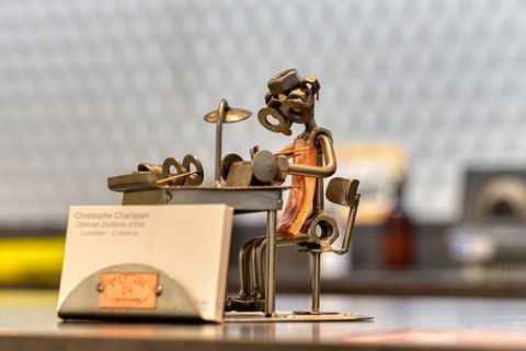petite sculpture porte-carte, représentant un petit homme fabricant des lunettes. Il est fait de vis, de clous et de boulons, assis sur une chaise